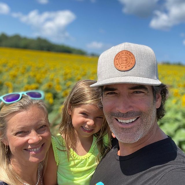 Flora Oosterhouse in a green t-shirt smiling with her father in a grey cap and black t-shirt and her mother in in blue framed goggles.